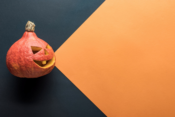 top view of spooky Halloween pumpkin on orange and black background - Фото, изображение