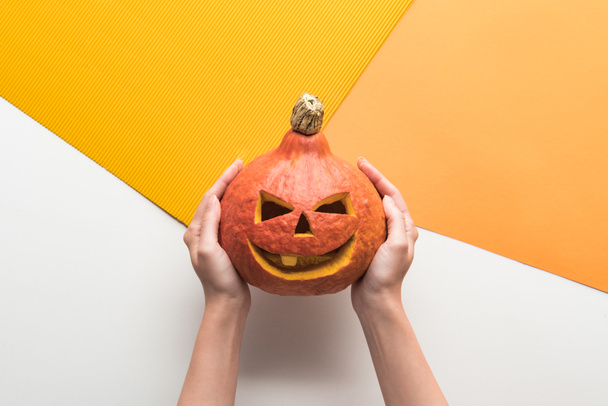 cropped view of woman holding Halloween pumpkin on white and orange background - Zdjęcie, obraz