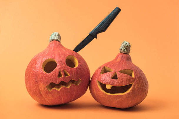 spooky Halloween pumpkins with knife on orange background - Foto, Bild