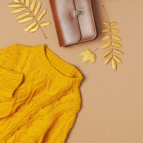 Damentasche aus braunem Leder, orangefarbener Strickpullover, goldenes Herbstblatt auf braunem Hintergrund, flache Lagekopierfläche. modische Damenaccessoires. herbstliches Modekonzept. stilvolle Damenkleidung - Foto, Bild