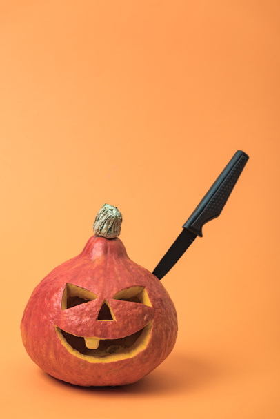 spooky Halloween pumpkin with knife on orange background - Fotografie, Obrázek