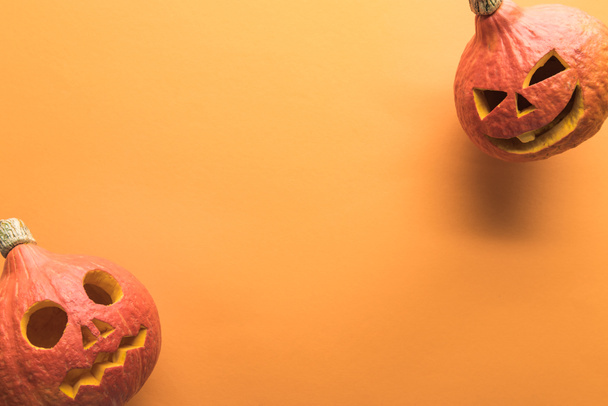 top view of carved spooky Halloween pumpkins on orange background with copy space - Fotó, kép