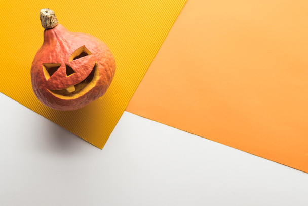 top view of carved spooky pumpkin on white and orange background - Fotoğraf, Görsel