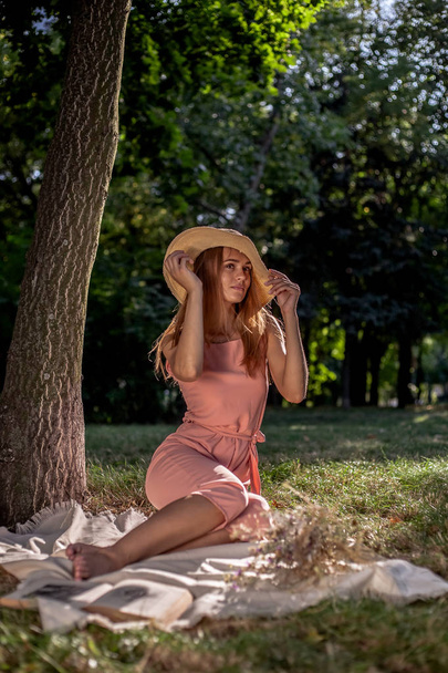 Belle fille reposant sur l'herbe près de l'arbre. Dans un chapeau avec un livre de fleurs séchées et un smartphone
. - Photo, image