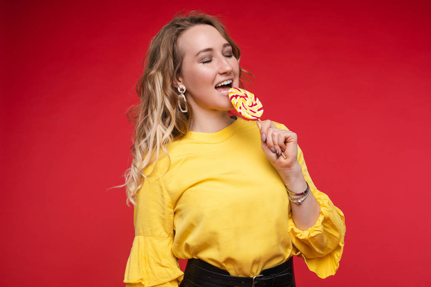 Girl eating delicious lollipop on red isolated background - Photo, Image