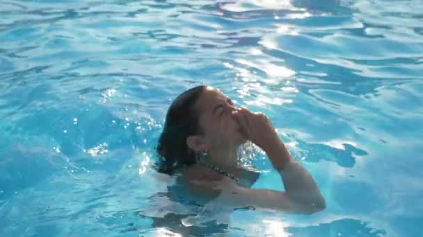 Jonge vrouw coming out of water houden haar neus in het zwembad in slo-mo originele weergave van een mooie jonge vrouw met lange losse haren naar boven en het nemen van haar neus in een peuterbad met sprankelende blauwe wateren in slow motion. - Video