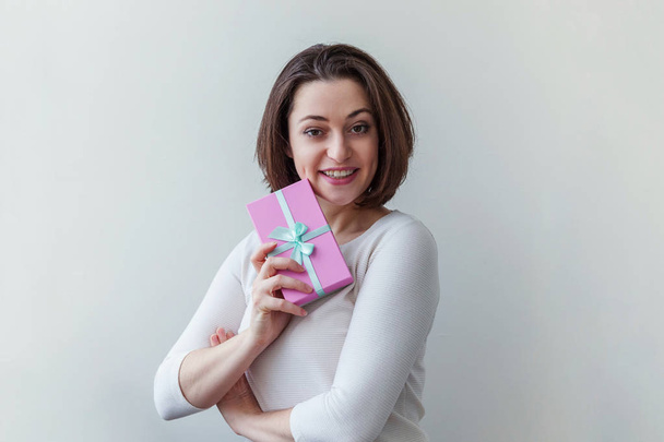 Jonge positieve vrouw houden kleine roze geschenk doos geïsoleerd op witte achtergrond. Voorbereiding voor vakantie. Meisje op zoek gelukkig en opgewonden - Foto, afbeelding