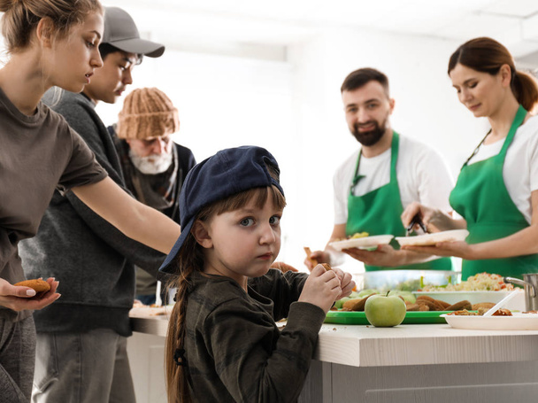 Niña con gente pobre recibiendo comida de voluntarios en el interior
 - Foto, Imagen