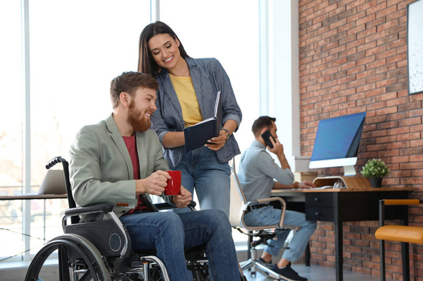 Young man in wheelchair with colleagues at office - Фото, изображение
