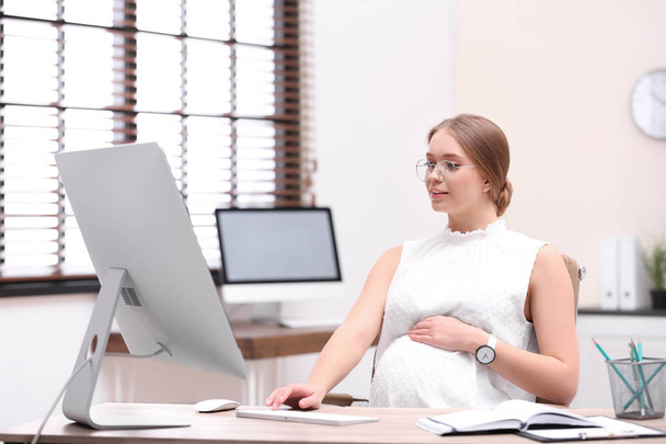 Young pregnant woman working with computer at table in office - Φωτογραφία, εικόνα