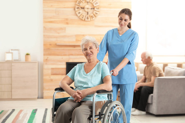 Nurse assisting elderly woman in wheelchair at retirement home. Space for text - Photo, Image