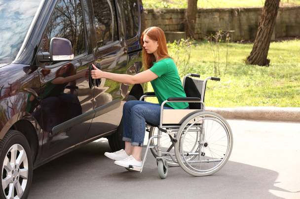 Woman in wheelchair opening door of her van outdoors - Фото, изображение
