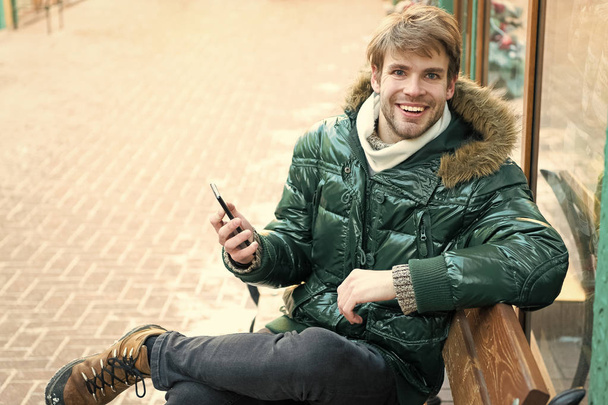 Man with phone. It is cold outside. Forest in snow. Fresh air. Snowy weather. Trendy winter coat. Winter fashion. Warm clothes. Happy man on winter holidays. Message from friend - Photo, image