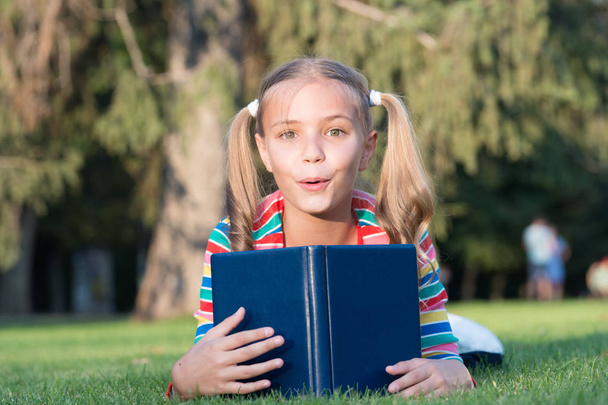 愛らしい本の虫。学校の時間だ積極的に成長し、達成している思いやりのある学習者を開発します。小さな子供が本を読んでる緑の芝生をリラックスした物語を読む女子高生。かわいい生徒は読書を楽しむ - 写真・画像