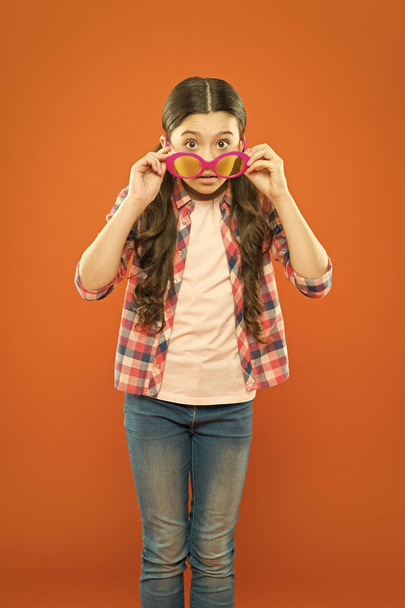 She is a smart one. Little smart girl on orange background. Adorable child with smart look through fancy glasses. Fashionable small kid wearing smart glasses - Foto, Imagem