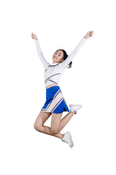 Pretty cheerleader smiles and jumps on the studio - Фото, зображення