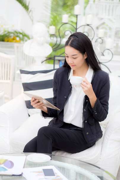 Молодая бизнесвумен азиатка сидит за столом глядя планшет и хо
 - Фото, изображение