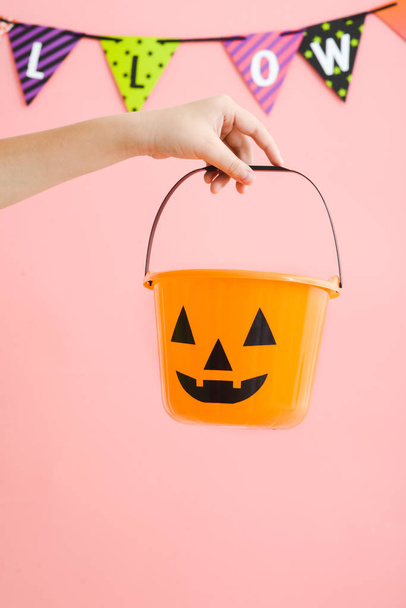 Kid's hand holding orange pumpkin plastic bucket with pink backg - 写真・画像