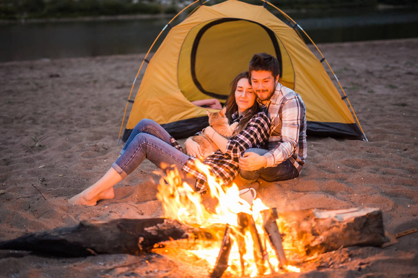 People, tourism and nature concept - Man and woman with their cat sit near a fire - Photo, Image