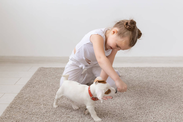 ペット、子供、動物コンセプト - ジャック ラッセル テリアの子犬が付いている床で遊ぶ幼い子供女の子 - 写真・画像