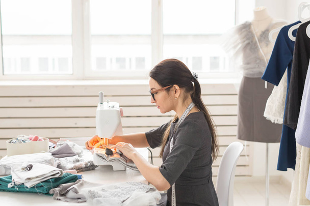 Mensen en mode concept - jonge naaister vrouw naait kleren op de naaimachine - Foto, afbeelding
