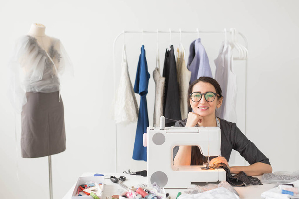Gente y concepto de moda - Mujer modista joven cose ropa en la máquina de coser
 - Foto, Imagen