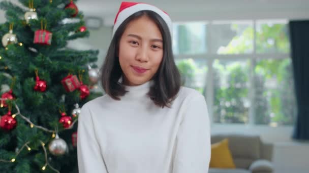 Asyalı kadınlar Noel festivalini kutluyor. Kadın genç Noel şapkası giymek mutlu kamera bakarak rahatla xmas kış tatilleri birlikte evde oturma odasında. - Video, Çekim