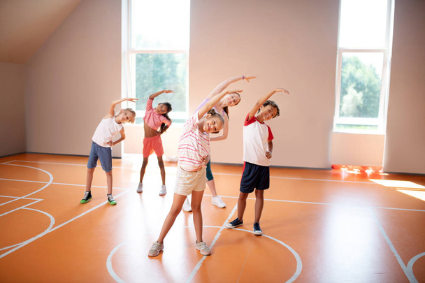 Boys and girls stretching with teacher at the PE lesson - Foto, Imagem