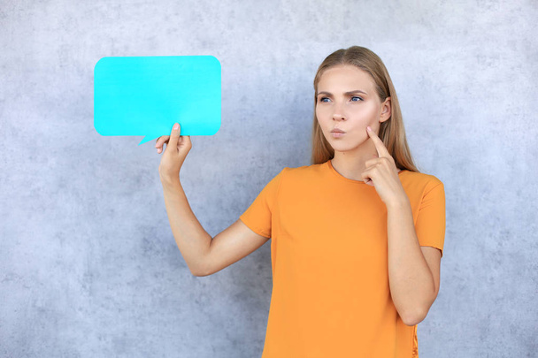 Beautiful young blonde woman standing isolated over gray background, holding empty speech bubble - Фото, зображення