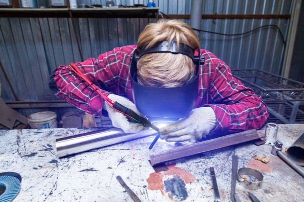 Young guy welder in a checkered red shirt welds a stainless stee - Foto, immagini