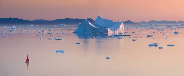 Megrekedt jéghegyek a ködben az Ilulissat melletti Jégkord torkolatánál. Grönland természete és tájai. Utazás a hajón a jég között. A globális felmelegedés jelensége. Partot a naplementében.  - Fotó, kép