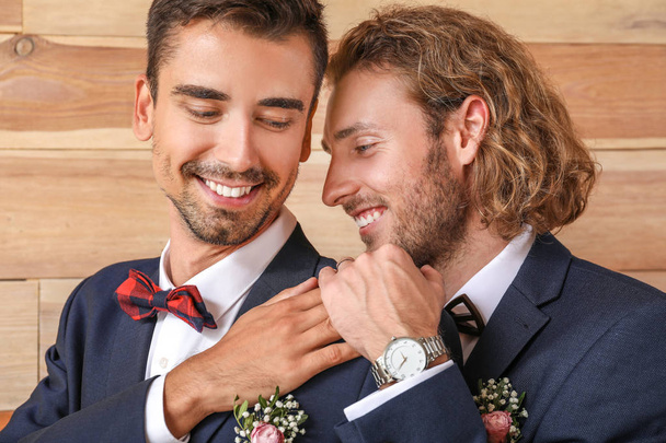 Portrait of happy gay couple on their wedding day against wooden background - 写真・画像