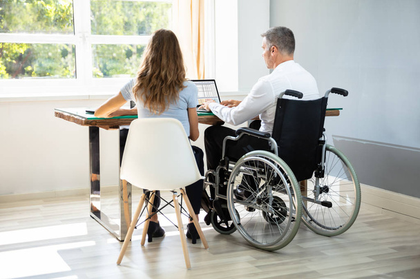 Disabled Businessman Sitting With His Partner With Laptop Over Desk In Office - Zdjęcie, obraz