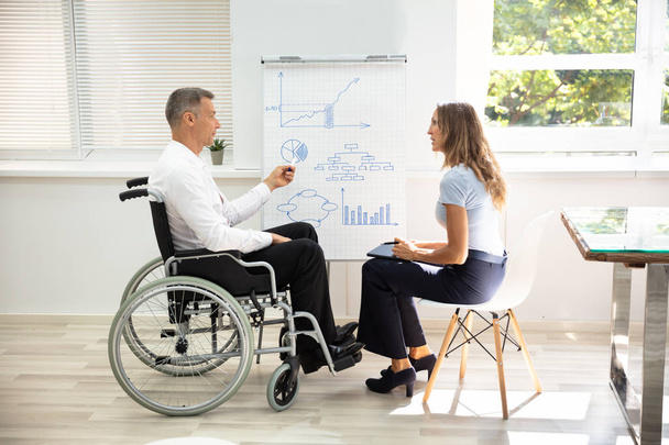Disabled Matured Businessman Showing Diagram While Giving Presentation To His Colleague In Office - Valokuva, kuva