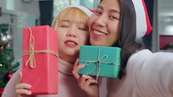 Asian Lesbian couple celebrate Christmas festival. LGBTQ female teen relax happy holding Gift and using smartphone selfie with Christmas tree enjoy xmas winter holidays in living room at home. - Video, Çekim