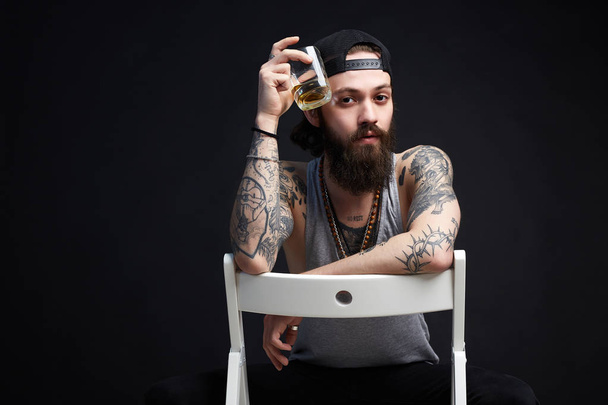 κομψό μούσι άνθρωπος με τατουάζ απολαμβάνοντας το ουίσκι - Φωτογραφία, εικόνα