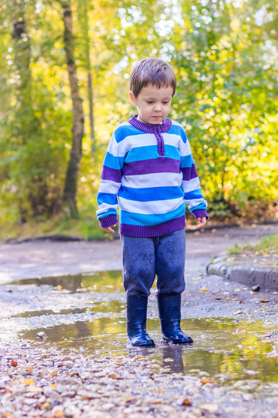 Un niño pequeño está saltando en un charco. Un chico con botas de goma. Feliz infancia. Puddles después de la lluvia. Noche cálida de verano
. - Foto, imagen