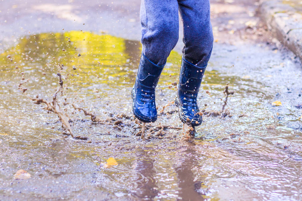 Un niño pequeño está saltando en un charco. Un chico con botas de goma. Feliz infancia. Puddles después de la lluvia. Noche cálida de verano
. - Foto, Imagen