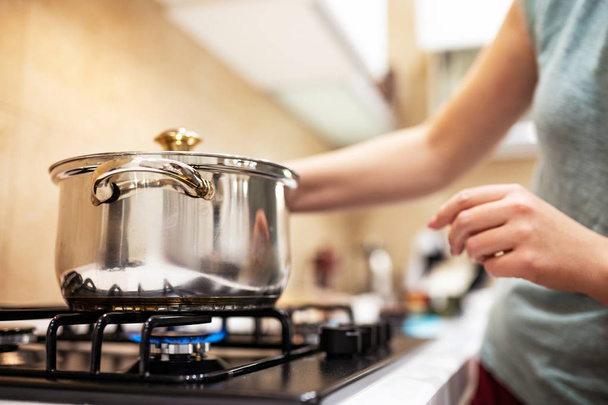 Beautiful young woman housewife prepairing dinner, hold in hands big steel saucepan, standing it on gas-stove. - Foto, Bild