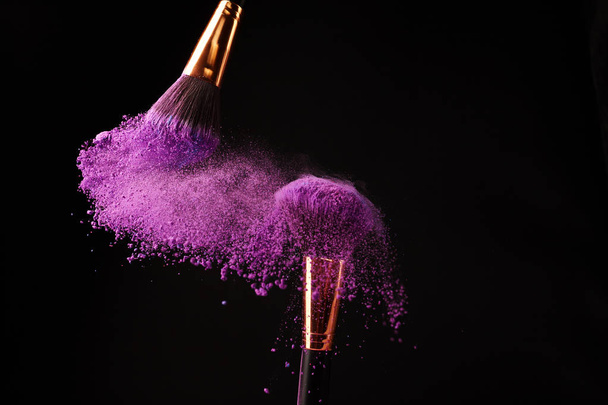 Make-up brushes with purple powder explosion on black background - Photo, image