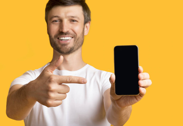 Muž držící telefon Smartphone ukazující prstem na obrazovku, žluté pozadí - Fotografie, Obrázek