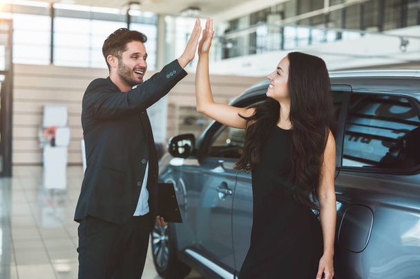 handsome man manager and beautiful brunette woman client standing near brand new car after succesful deal in dealership center - Fotoğraf, Görsel