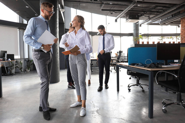 Gruppe moderner Geschäftsleute spricht und lächelt, während sie im Büroflur steht - Foto, Bild