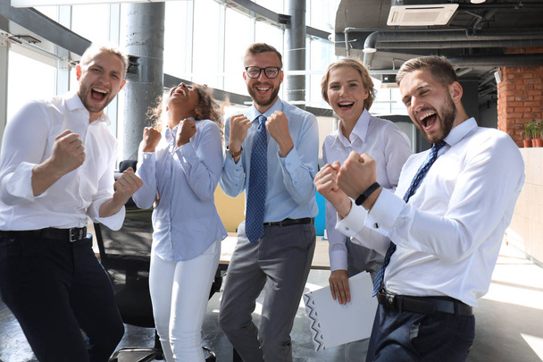 Пять счастливых современных бизнесменов держат руки поднятыми и радостными, стоя в большом офисе
 - Фото, изображение
