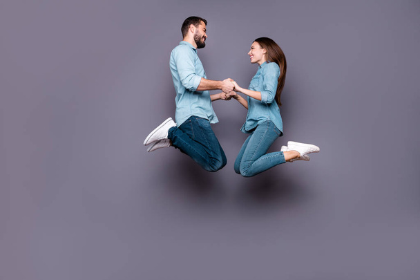 Full size photo of cheerful romantic students hold hand jump wear denim jeans isolated over grey background - 写真・画像