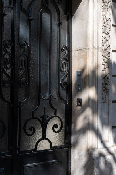 Czarne ozdobne kraty retro drzwi i rogu starożytnego kamienia marmuru budynku z rzeźbiarskich dekoracji. Streszczenie tła rozmyte cienie na drzwiach architektury klasycznej. Podróże Europa - Zdjęcie, obraz