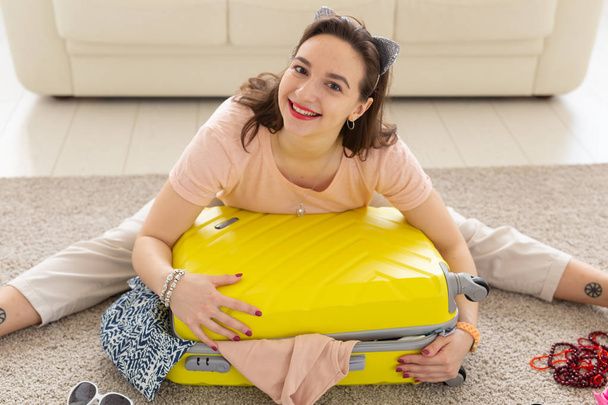 Vacaciones, viaje y concepto de viaje - Mujer joven recoge una maleta en casa en el dormitorio, un montón de cosas, vacaciones y maleta amarilla
 - Foto, Imagen