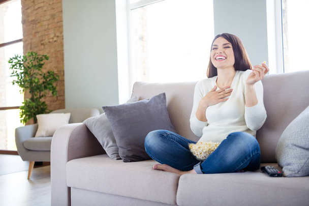 Portrait of her she nice attractive charming cheerful cheery glad positive woman sitting in lotus position on divan watching funny series eating snack corn in light white interior living-room indoors - Photo, image