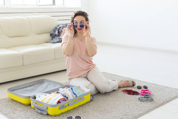 Tatil, yolculuk ve seyahat konsepti - Genç Kadın yatak odasında evde bir bavul toplar, bir çok şey, tatil ve sarı bavul - Fotoğraf, Görsel