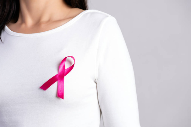 Nahaufnahme eines rosafarbenen Abzeichen-Bandes auf der Brust einer Frau zur Unterstützung der Brustkrebsbekämpfung. Gesundheitswesen, Medizin und Sensibilisierungskonzept für Brustkrebs. - Foto, Bild